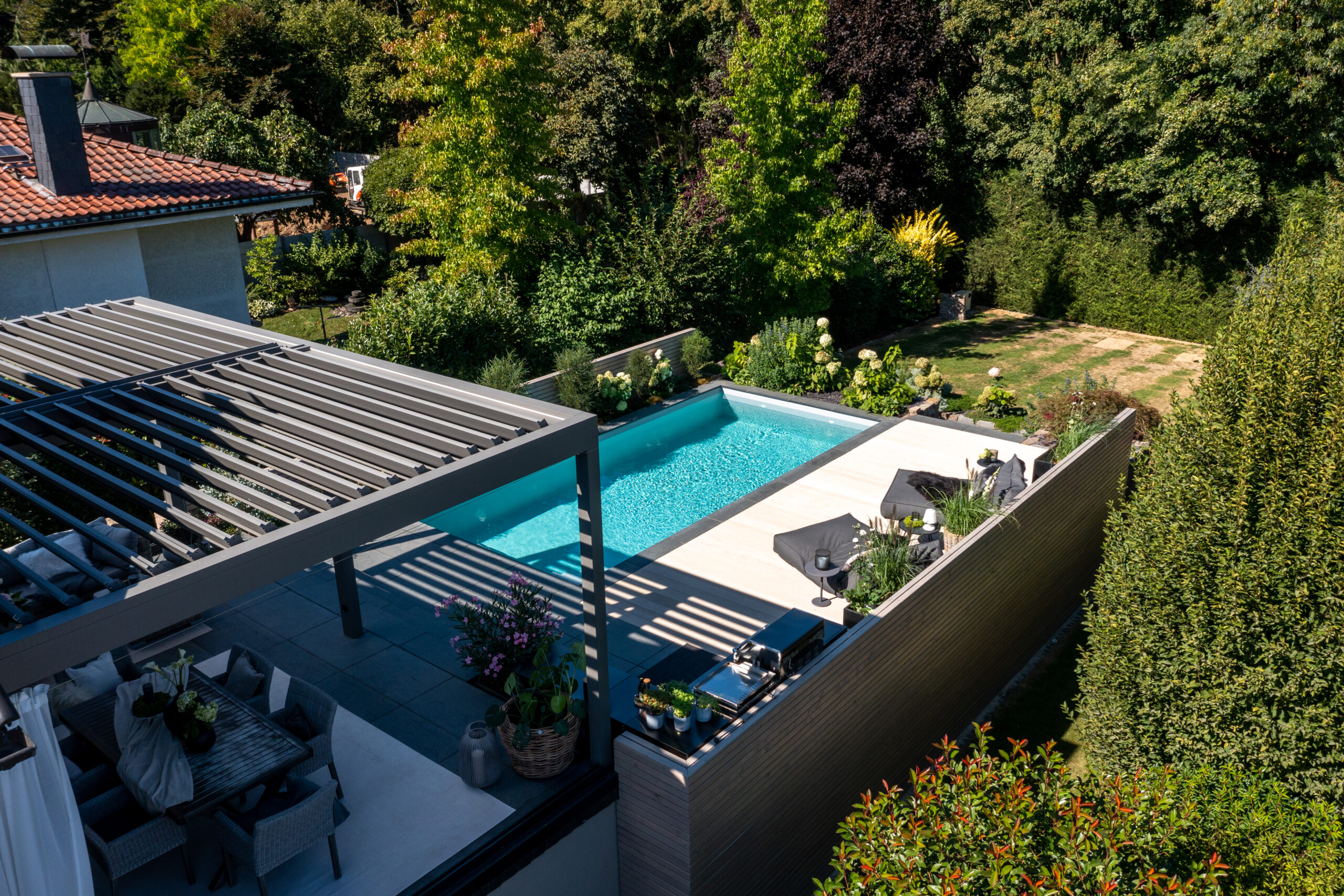 Pool vor überdachter Sitzecke mit Liegen und Haus im Sonnenschein