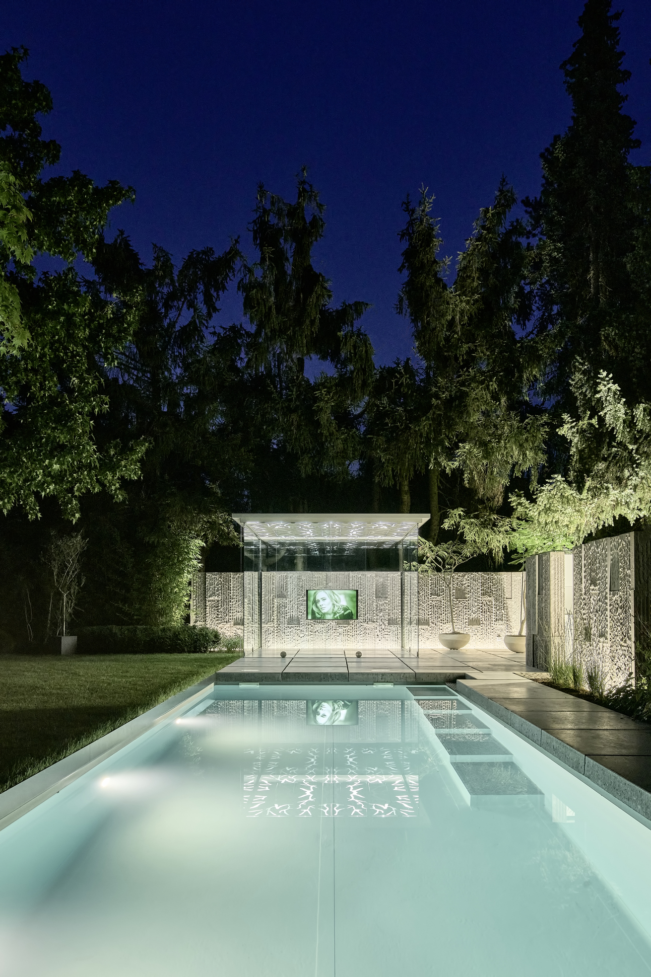 Glashaus mit Pool und Bildschirm im Garten bei Nacht