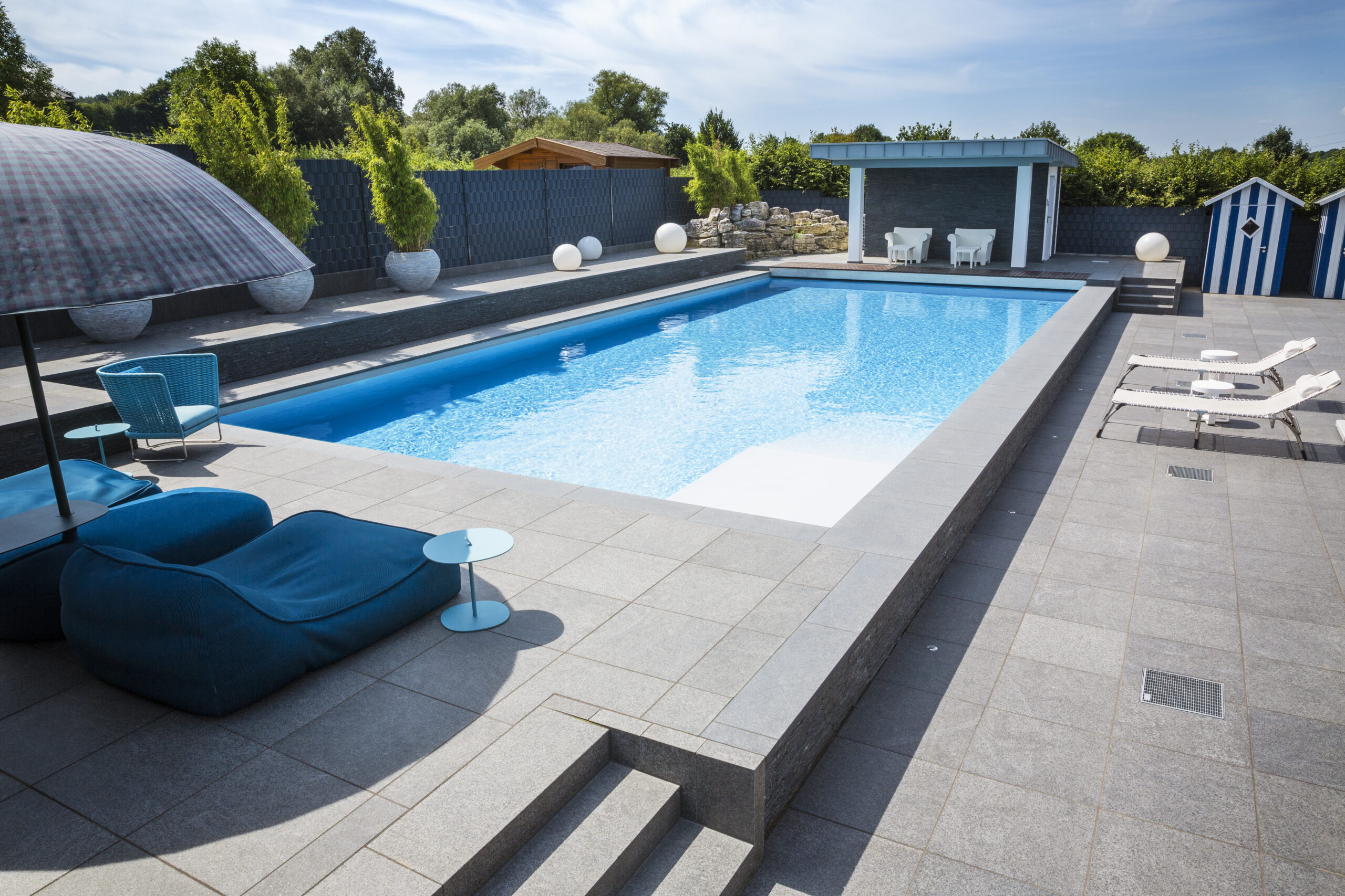 Schwimmbad vor Pavillon mit Sessel und Schirm im Sonnenschein