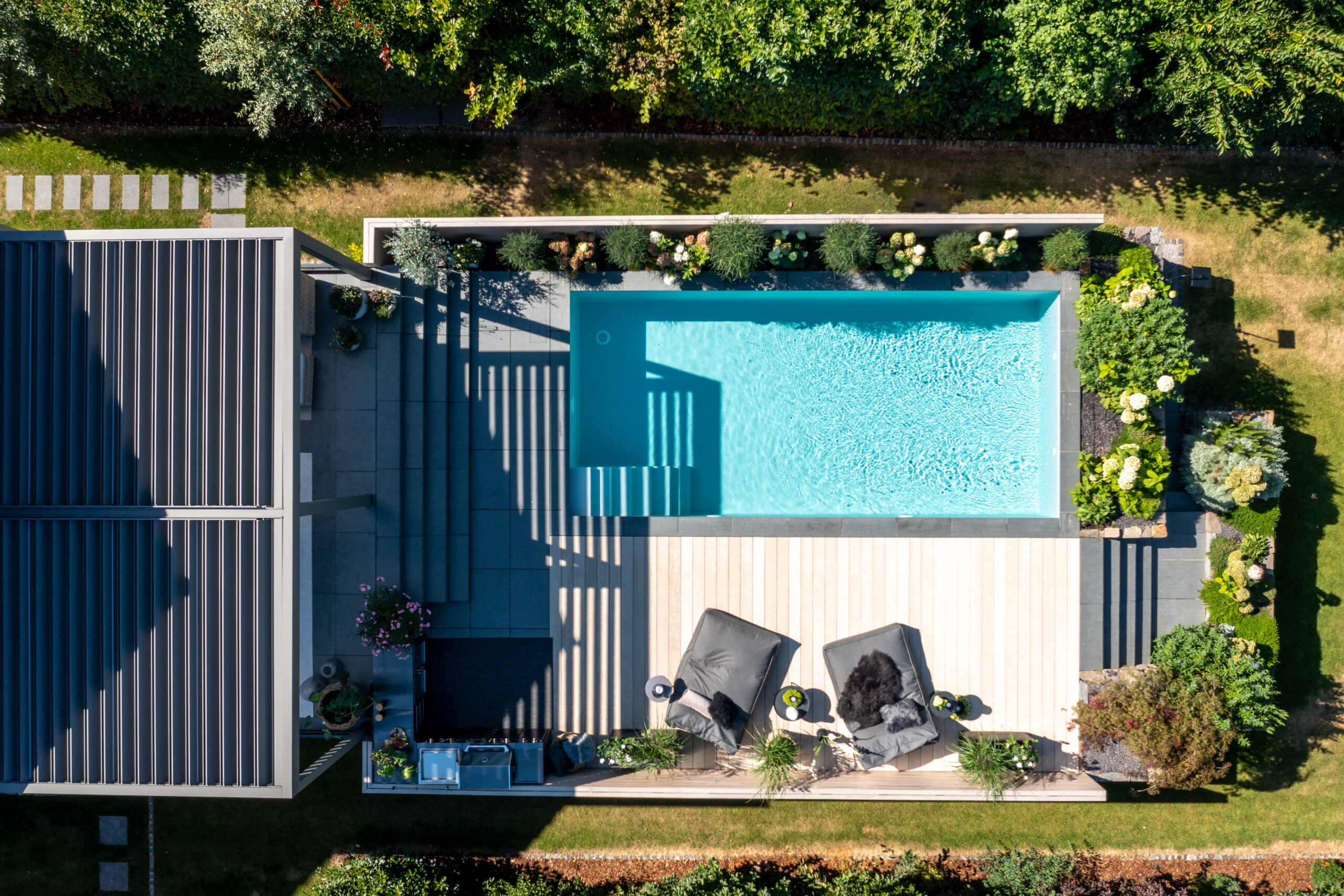 Pool vor überdachter Sitzecke mit Liegen und Haus im Sonnenschein von oben